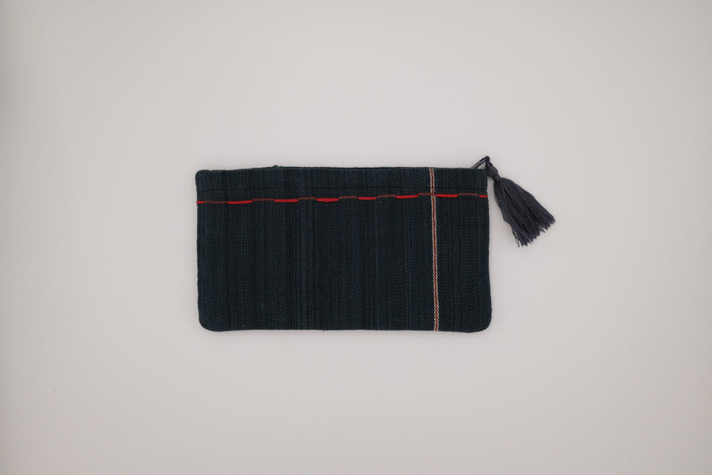 Black clutch bag with red trim and tassel on a light gray background