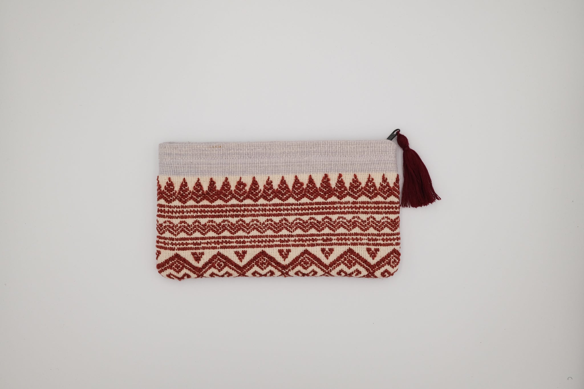 Pouch with red pattern and tassel on a light gray background